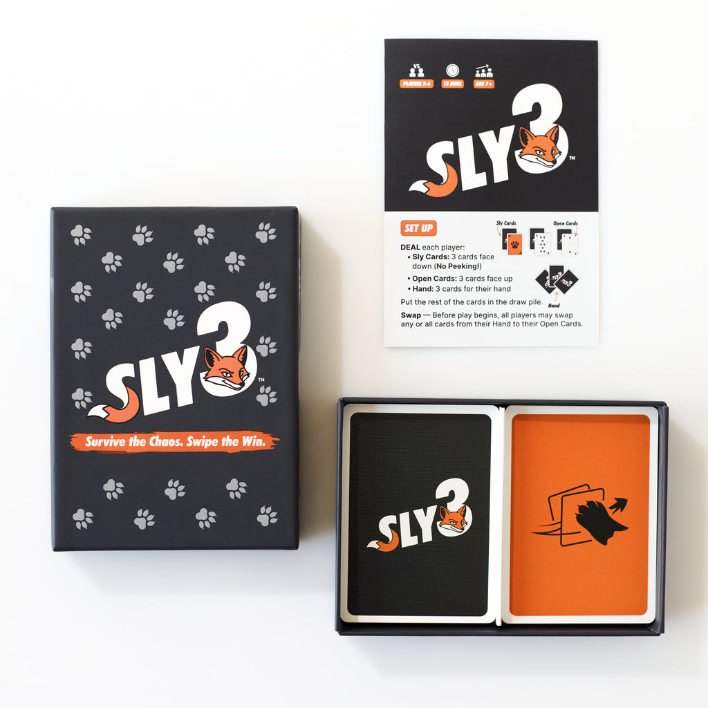 Sly3 card game set shown on a white background, including the black box with white paw prints, an instruction manual and the slogan 'Survive the Chaos. Swipe the Win.